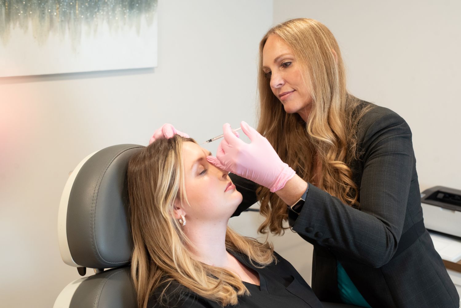 A woman receives a cosmetic treatment from a professional wearing pink gloves in a clinical setting.