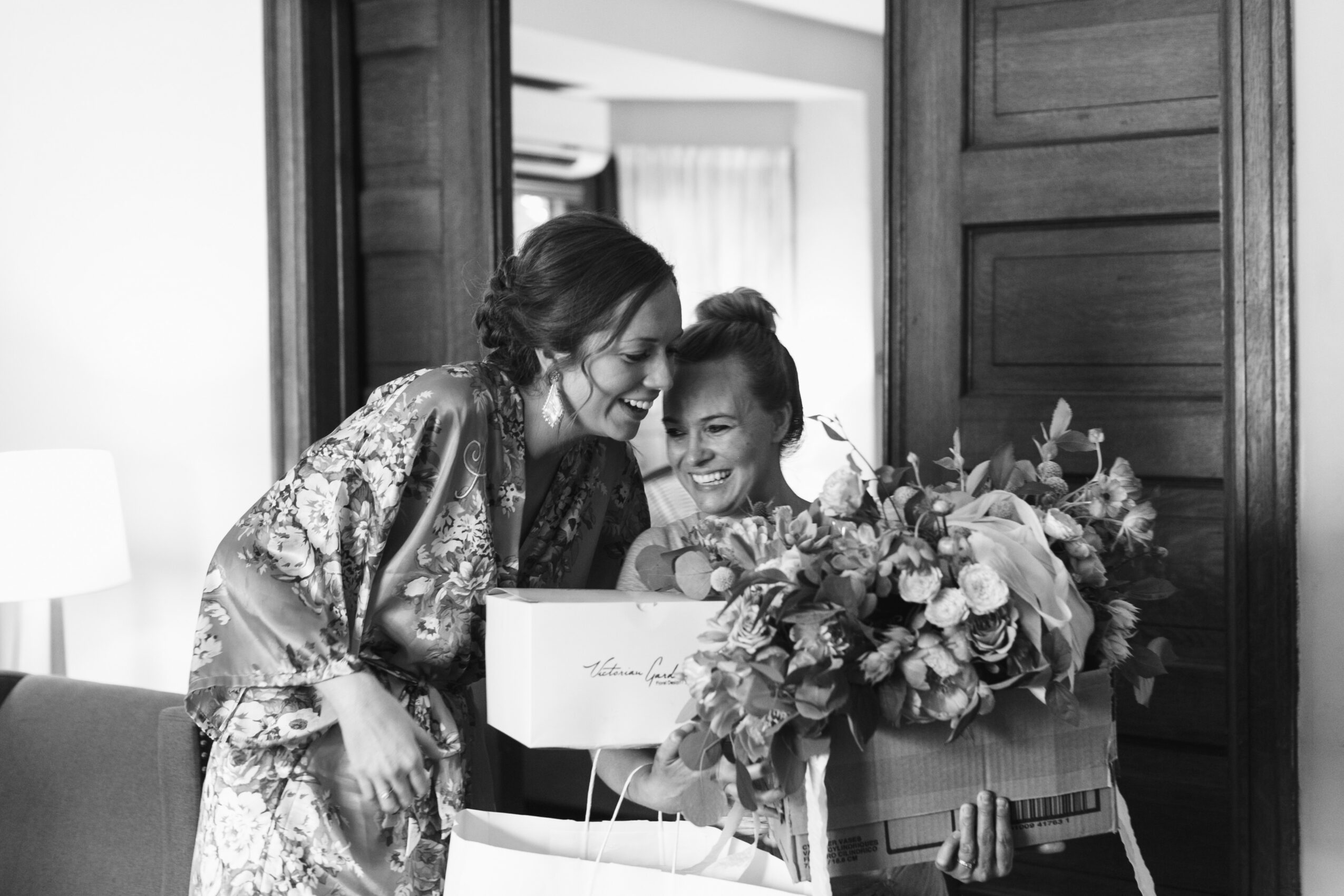 Two women smiling and looking at a large bouquet of flowers in a room with wooden paneling.