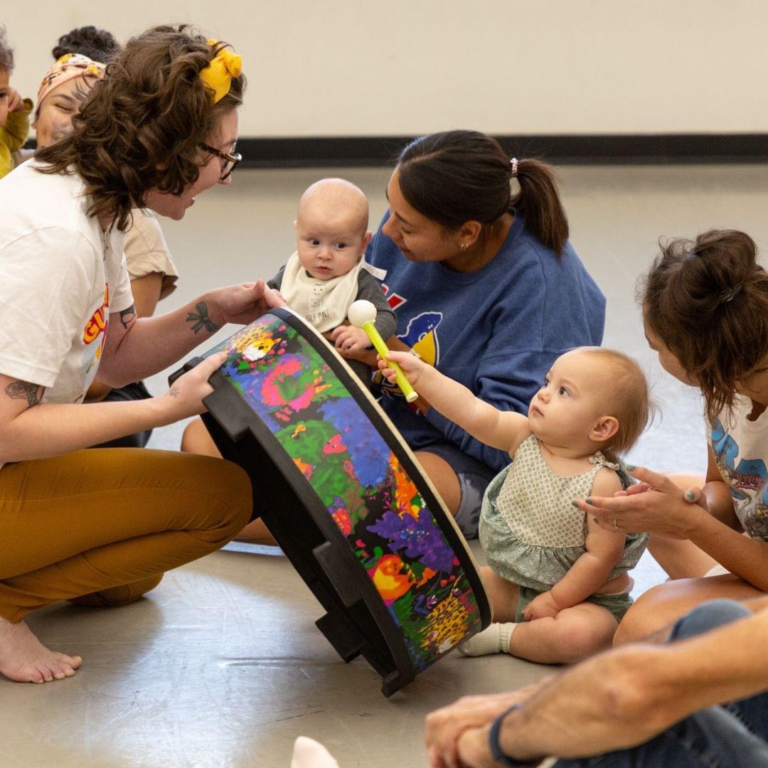 Adults and children gathered around a colorful, illuminated sensory toy on the floor, engaging with it in a room.