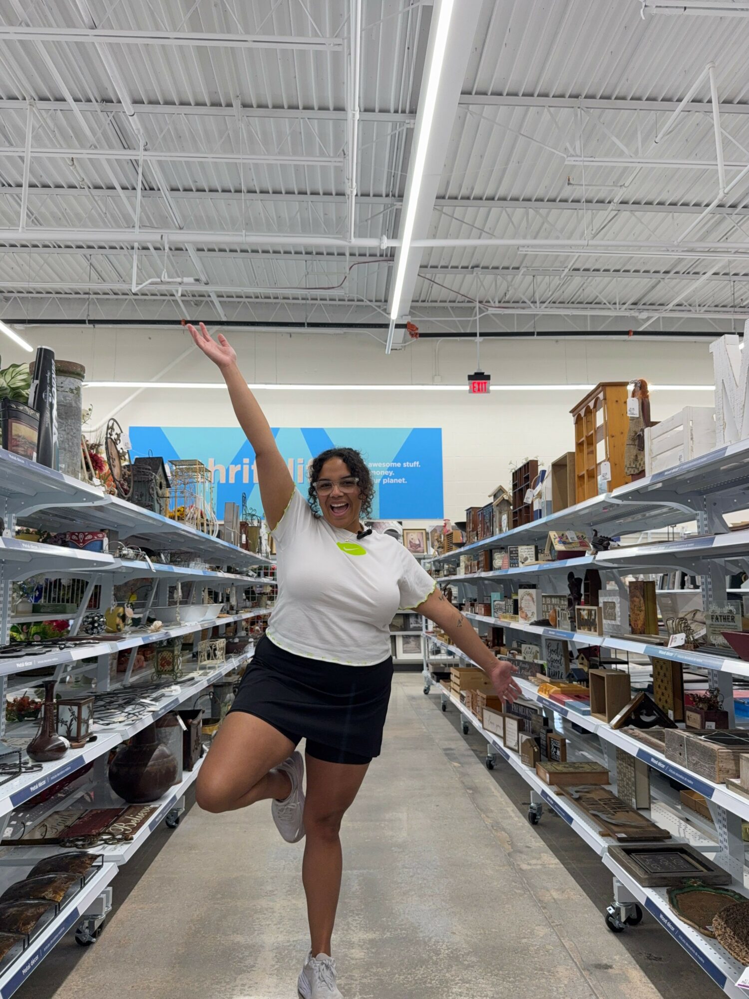 Woman shopping in a store aisle, reaching for an item on a high shelf, with shelves filled with products on both sides.