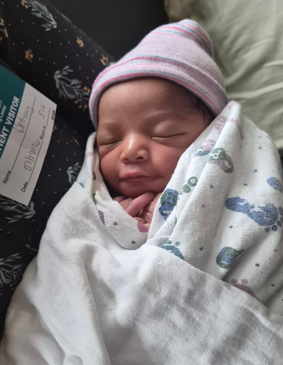 Newborn baby wrapped in a blanket, wearing a pink and white striped hat, sleeping peacefully.