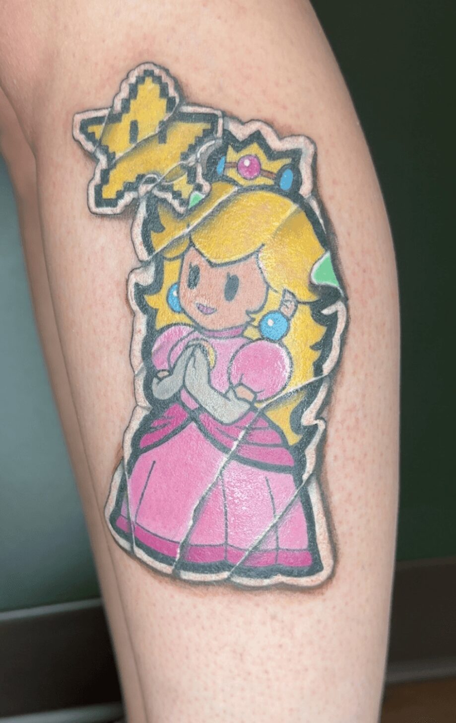 Tattoo of Princess Peach from Mario, with a star above her head, on a person's arm.