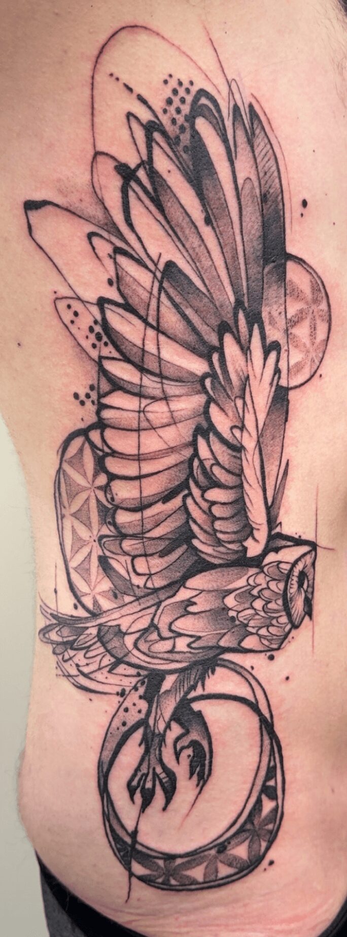 Detailed black and gray tattoo of a bird with wings spread, perched on a circular geometric design, on skin.