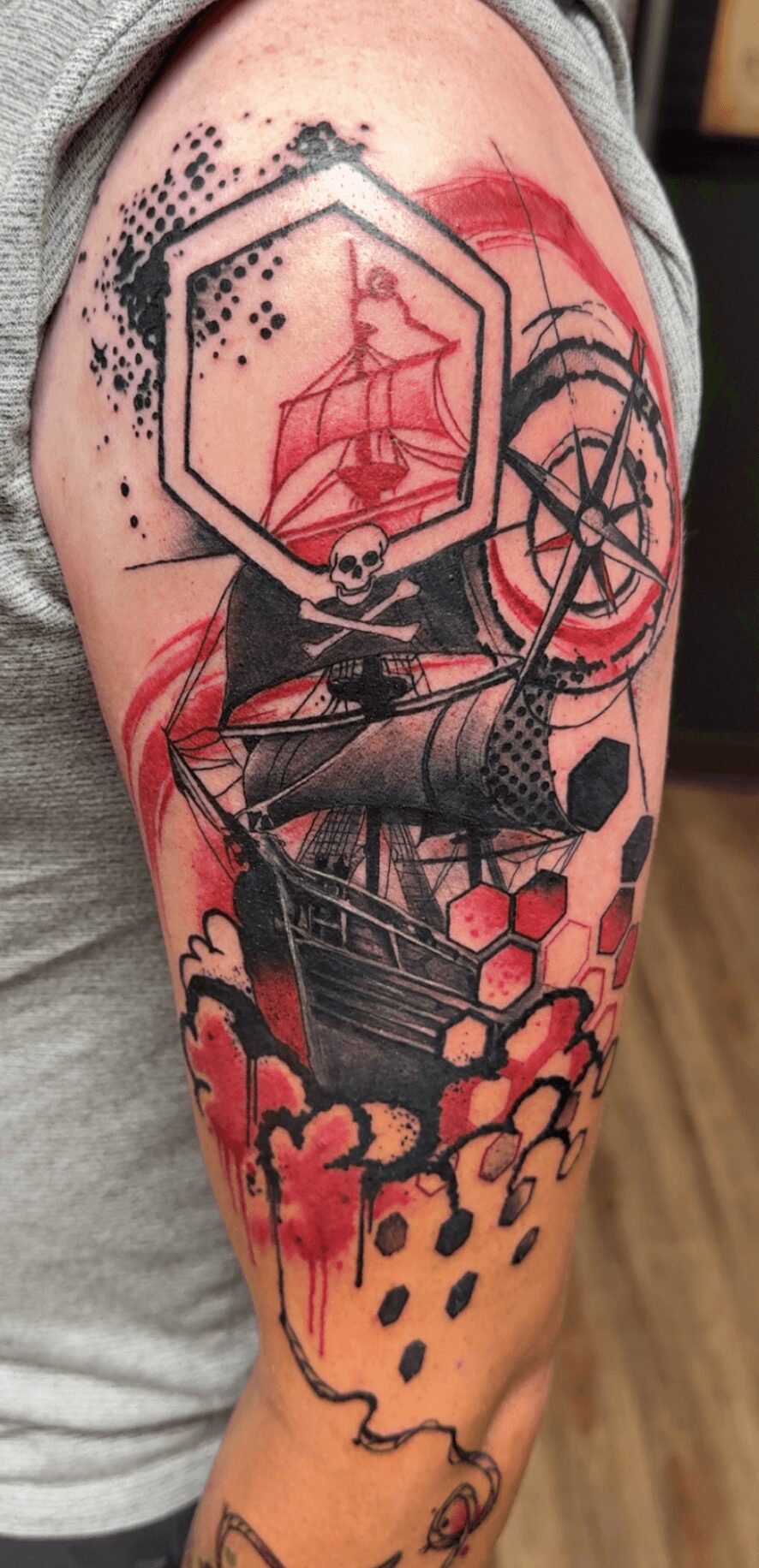 Tattoo of a ship with geometric shapes, a skull, and abstract elements on a person's arm.