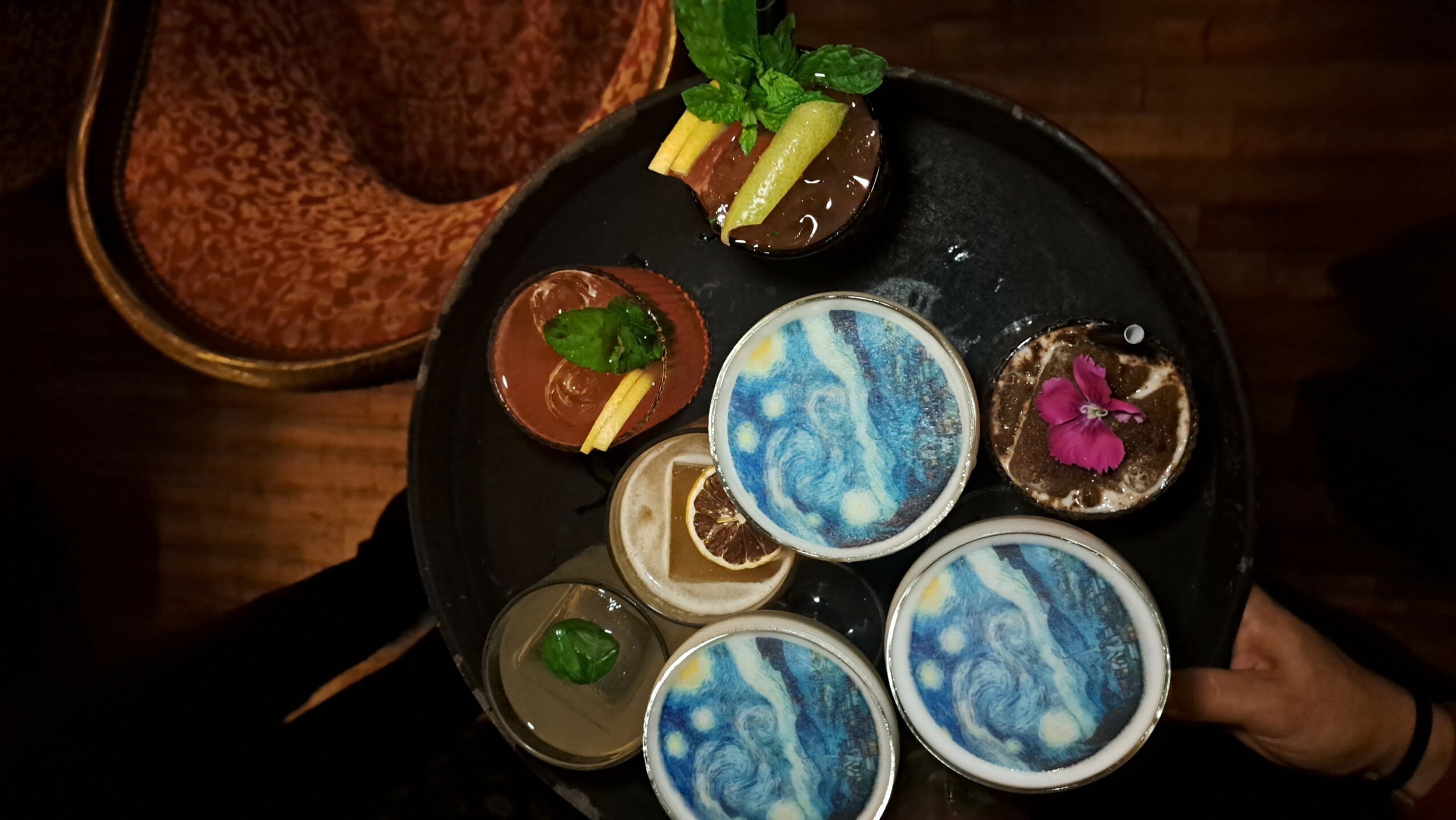 Tray with desserts, drinks, and garnishes on a dark surface, viewed from above.