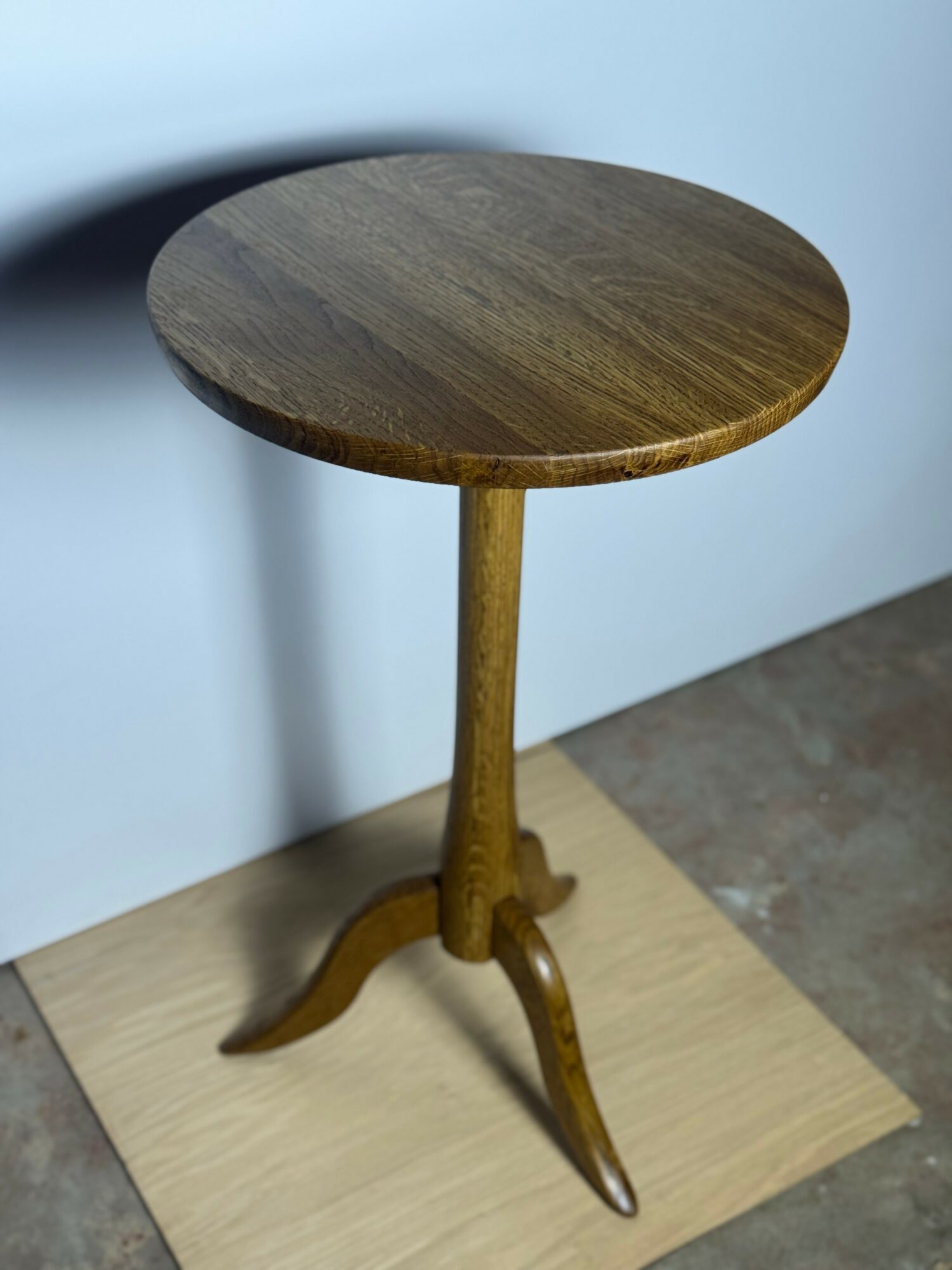 Wooden round table with a single central leg and curved base, placed on a light-colored surface against a light background.