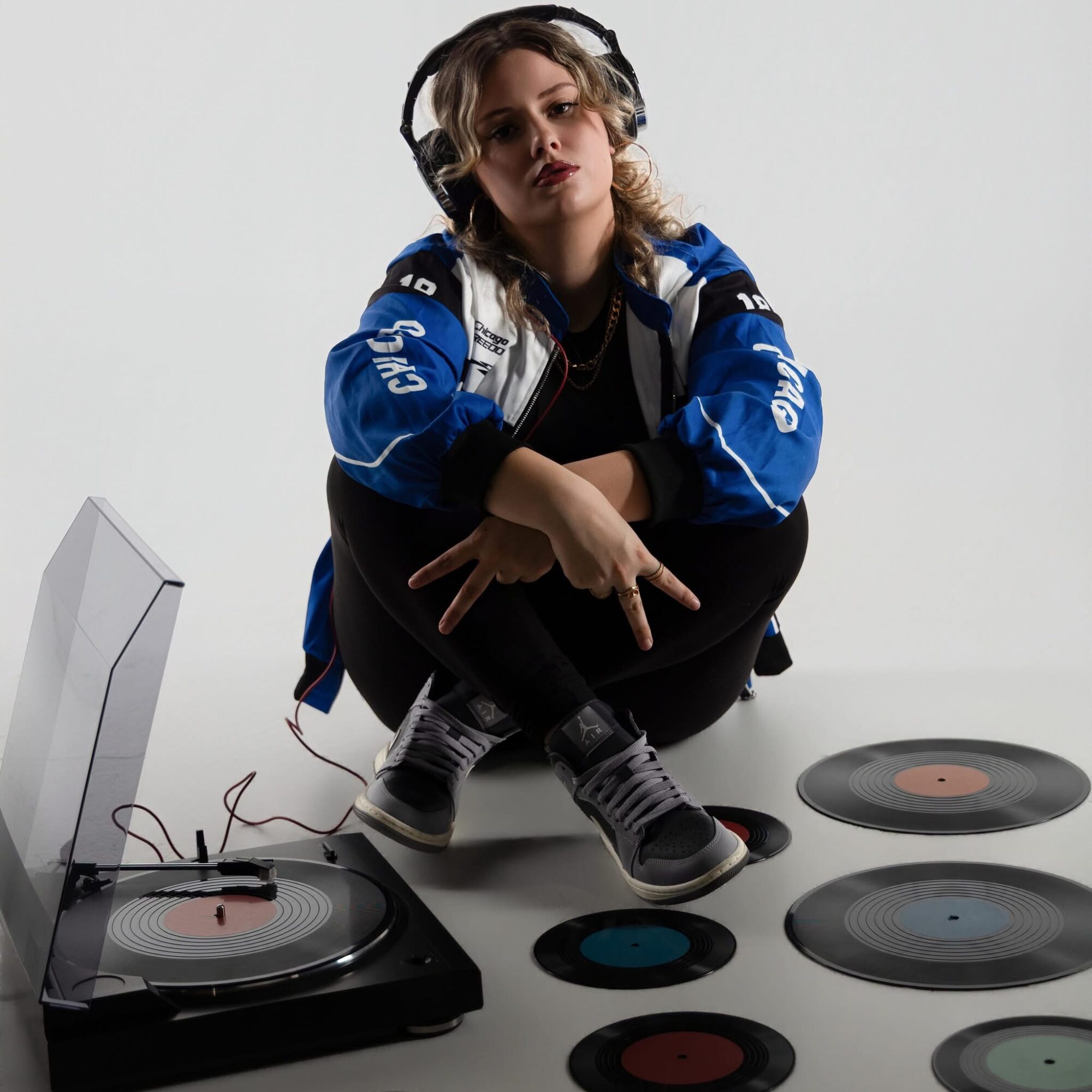 Person sitting on the floor with headphones, surrounded by vinyl records and a turntable, against a plain background.