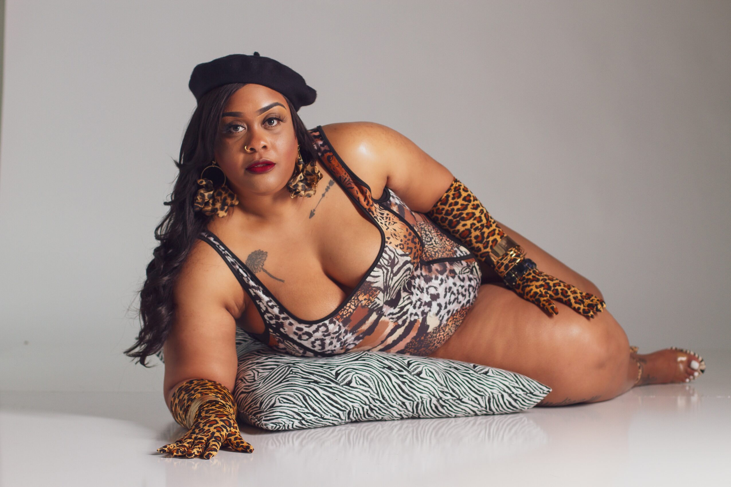 Woman lying on her side on a pillow, wearing animal print clothing and accessories, with a neutral background.