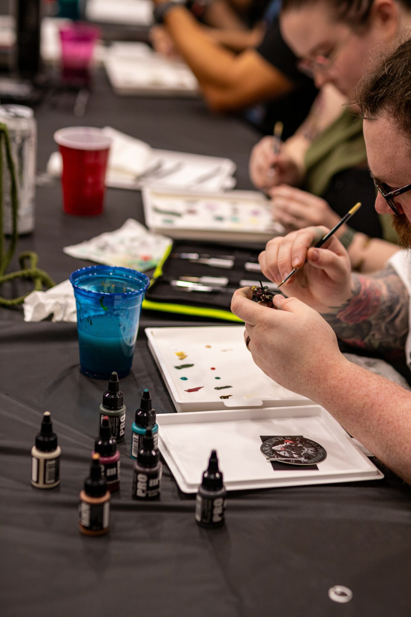 People working on tattoo designs at a table with ink bottles and paper, focusing on their artwork.