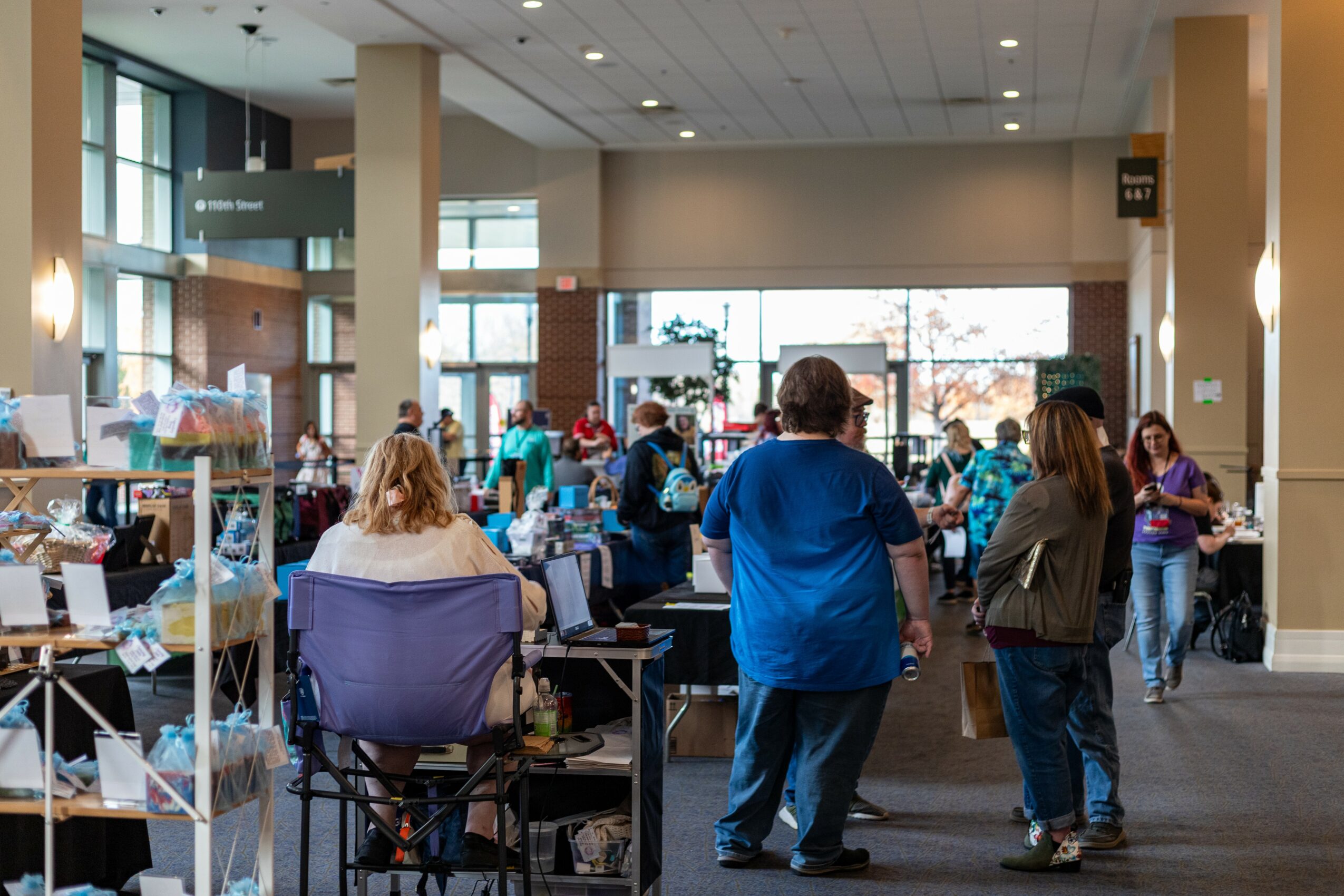 People shopping and browsing in a spacious indoor market with large windows and high ceilings.