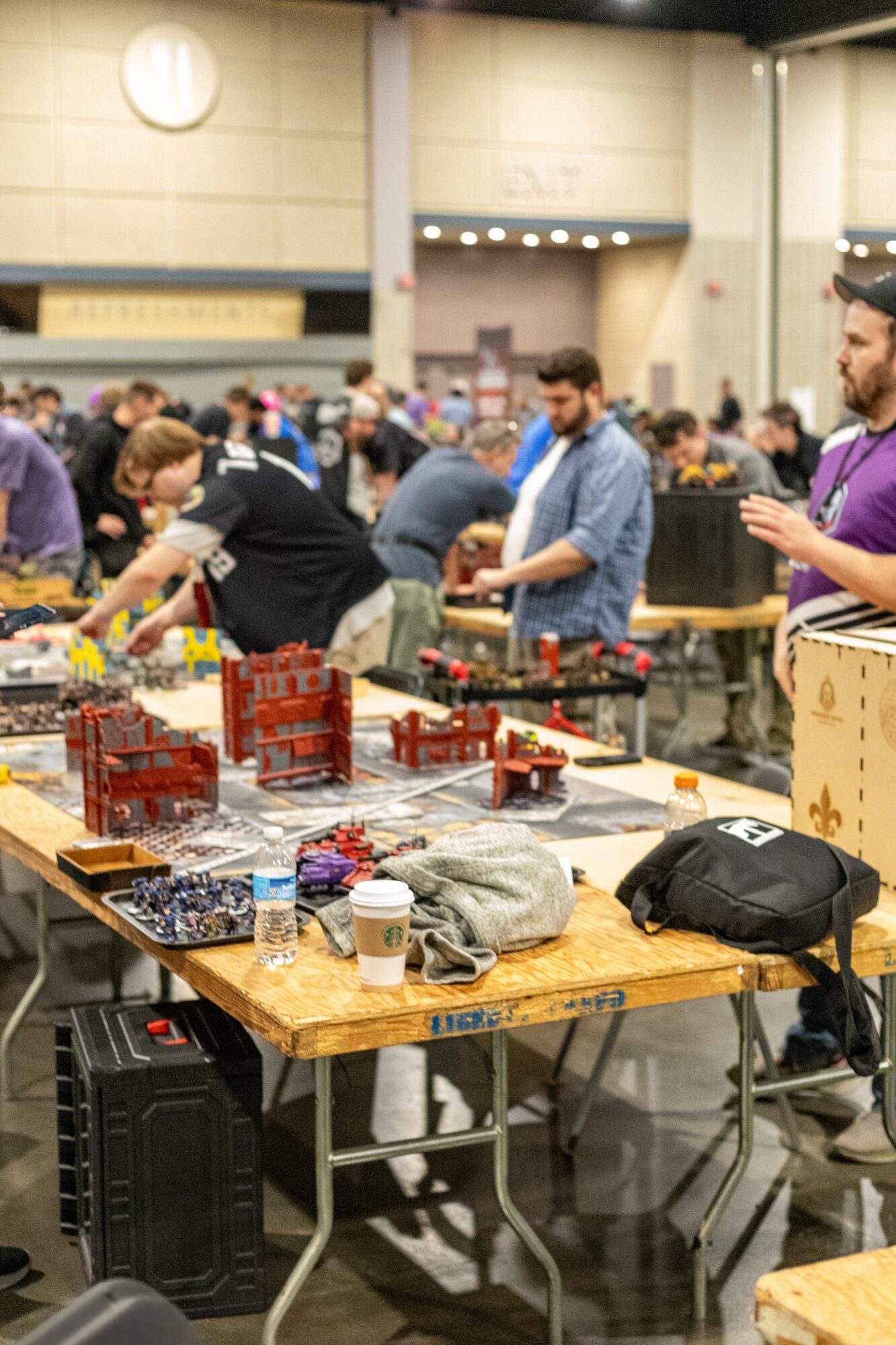People browsing and examining model train sets and accessories at a busy indoor event, tables filled with train items and supplies.