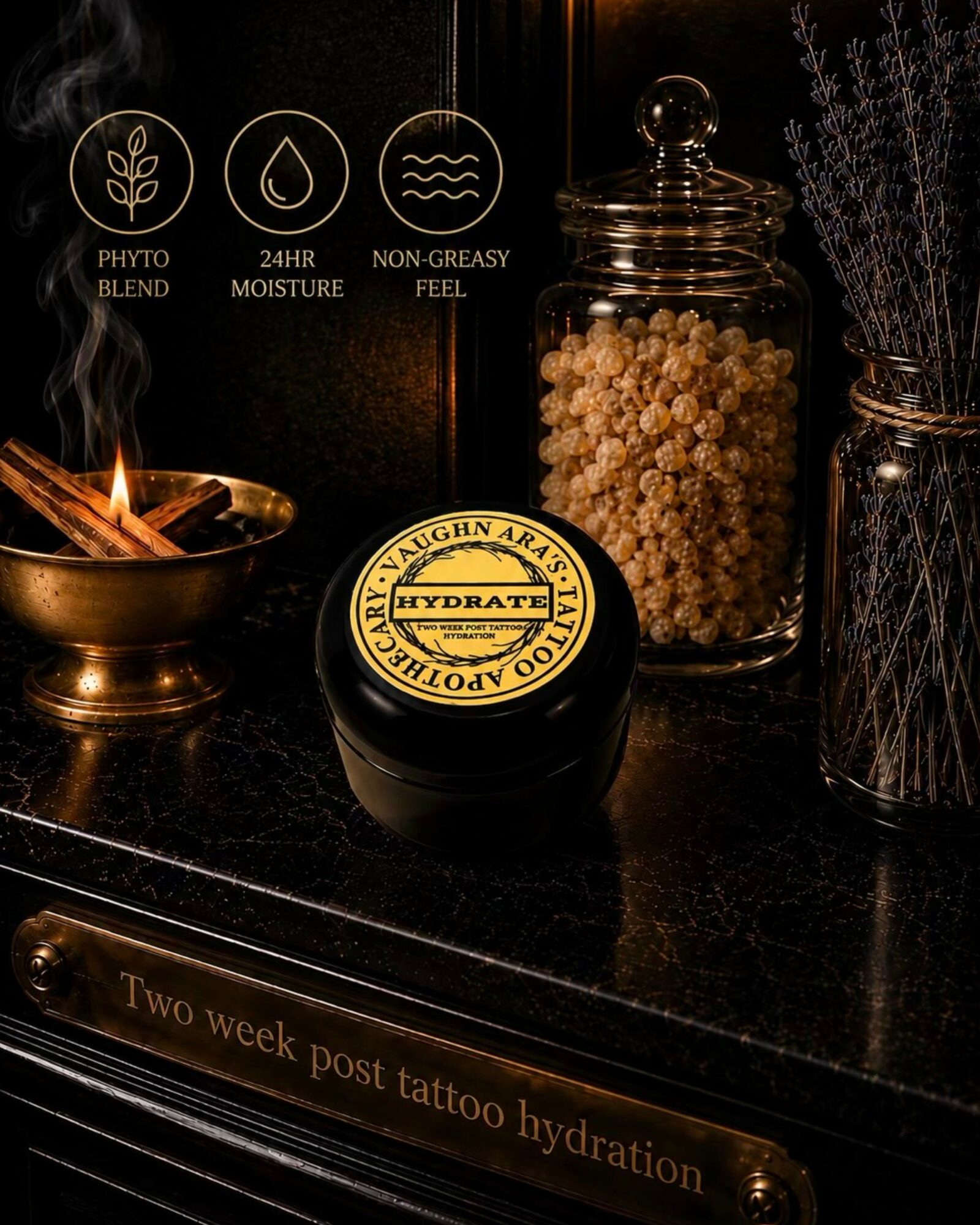 A black container with a yellow label, a glass jar with white beads, a bowl with a wooden spoon, and a vase with dried lavender on a black surface. Text on the surface reads 'Two week post tattoo hydration'.