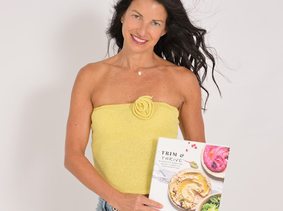 Woman with long dark hair wearing a yellow strapless top with a flower detail, holding a magazine, smiling.