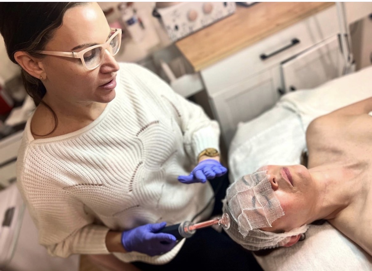 Medical professional prepares to give an injection to a patient lying in bed, wearing a cap and protective gear.
