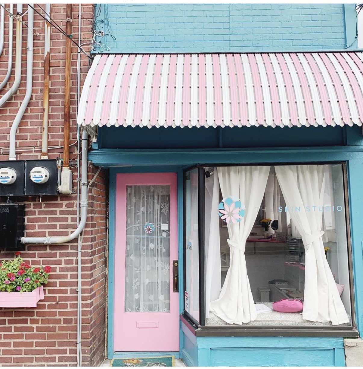 Storefront with pink door, blue walls, striped pink and white awning, and white curtains in the window.