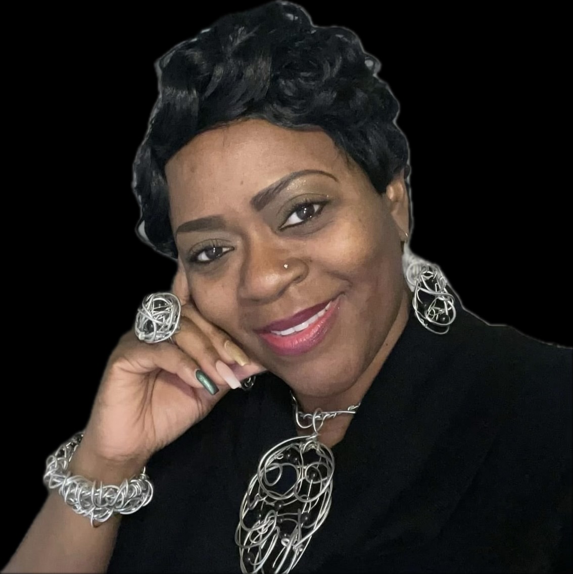 Woman with short black hair, wearing large silver jewelry, smiling, against a black background.