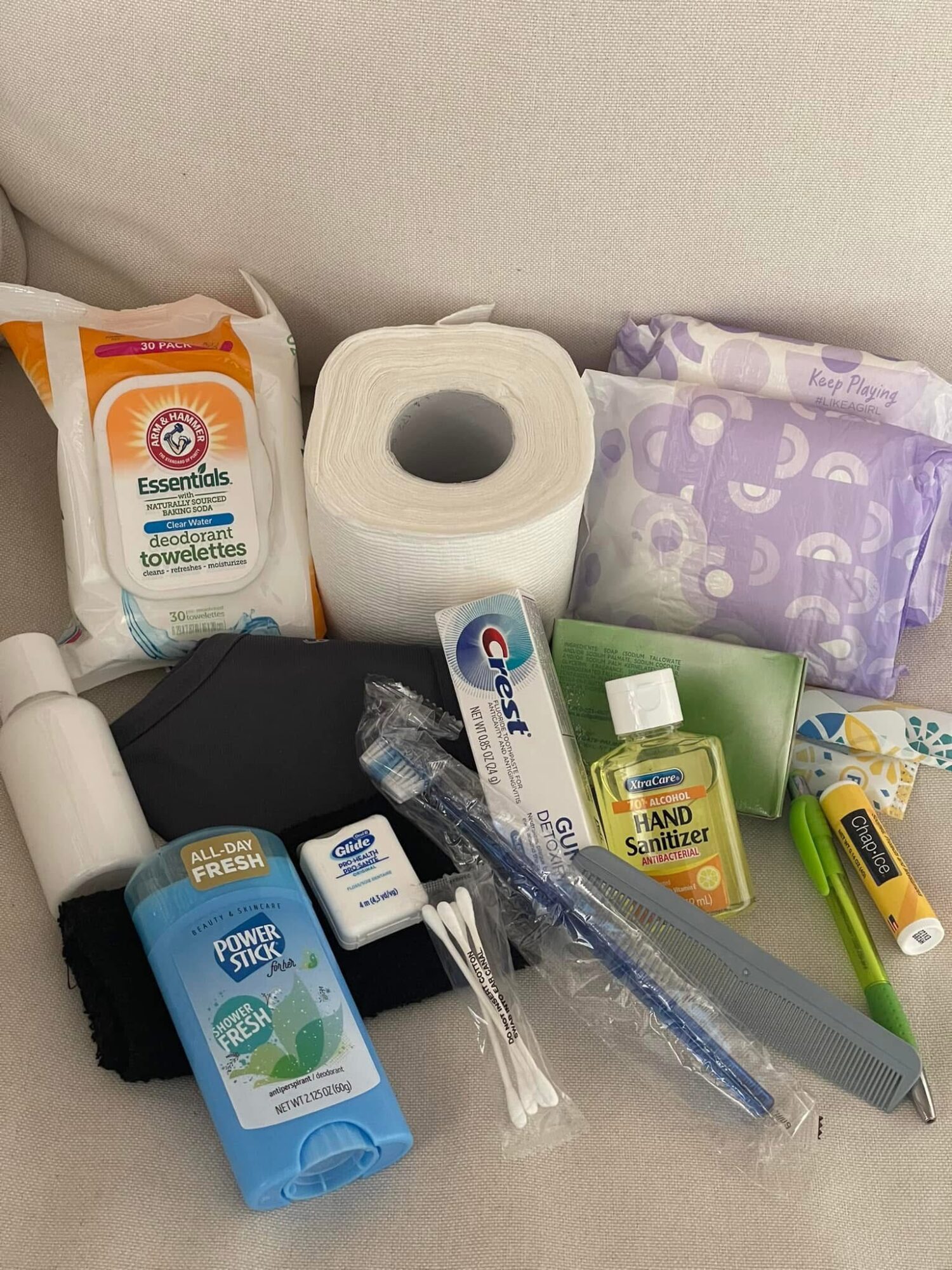 Collection of household items including toilet paper, tissues, hand sanitizer, wipes, and cleaning supplies on a surface.