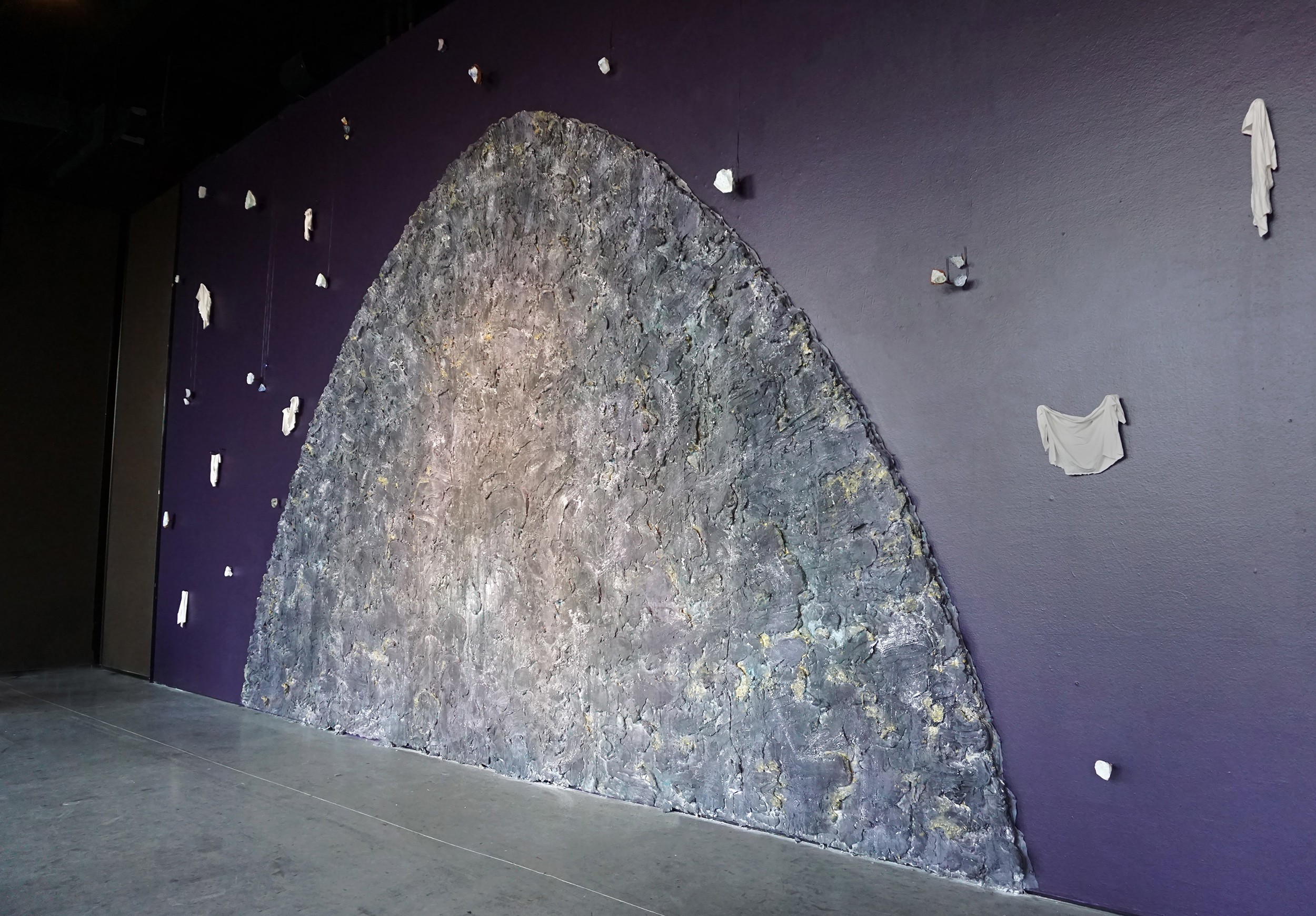 Wall with peeling paint and a large semi-circular textured surface, with scattered paint chips on a dark background.