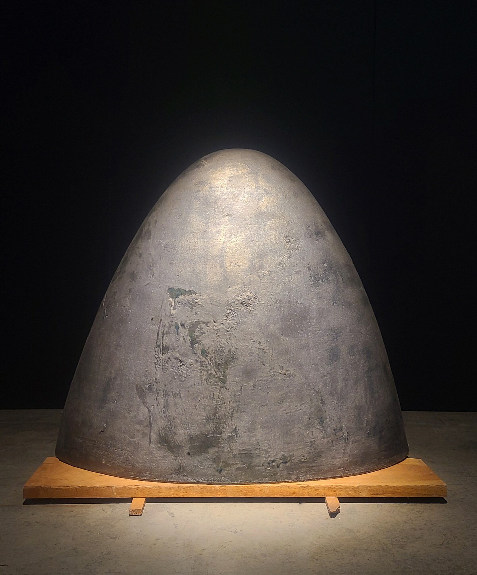 Large, rounded, gray stone sculpture on a wooden base against a dark background.