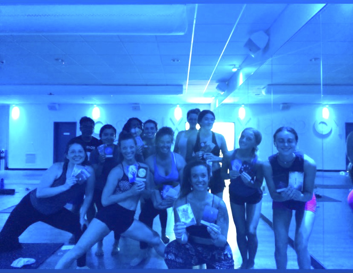 Group of people in a room with blue lighting, some holding certificates or awards, posing for a photo.