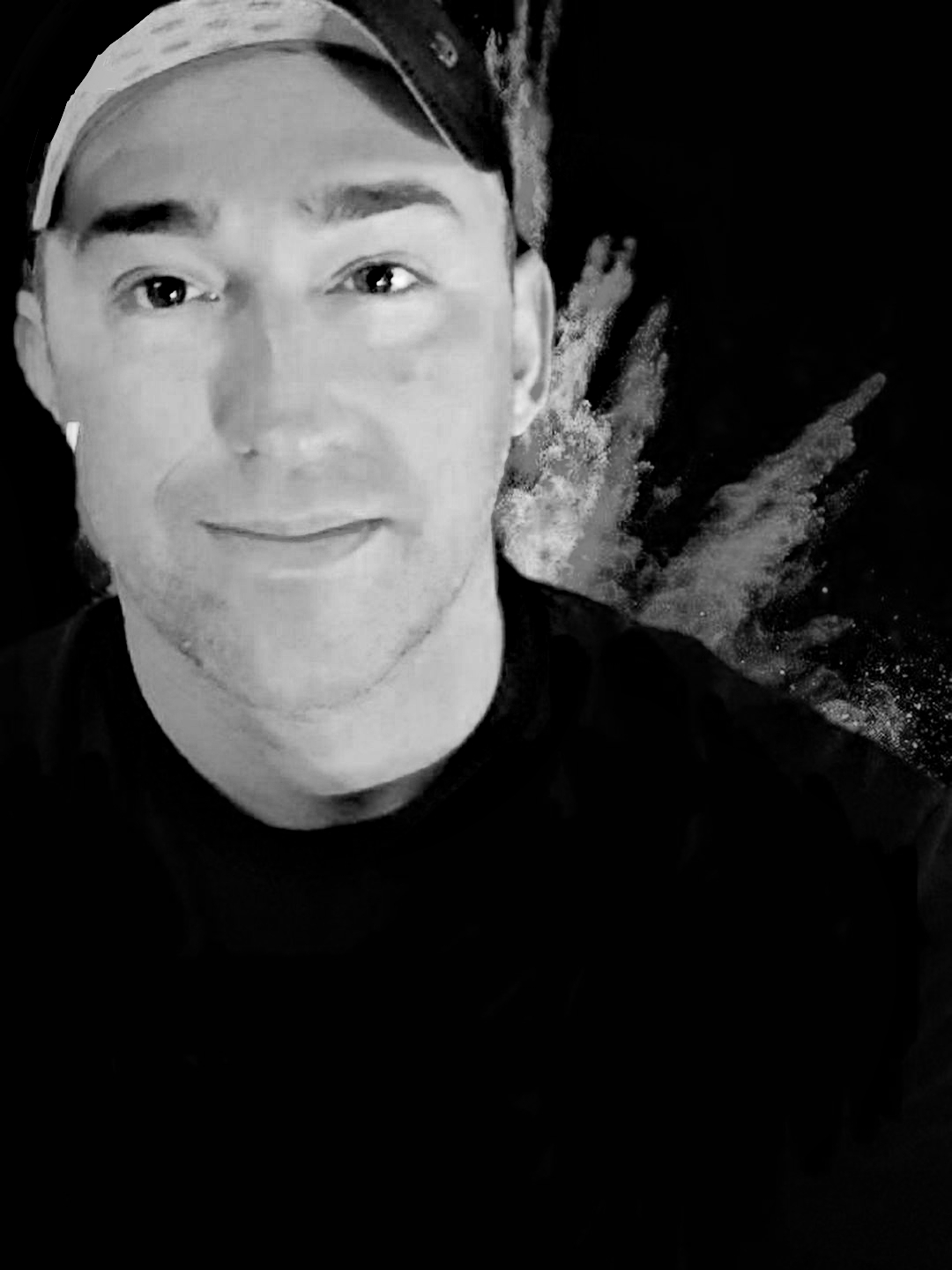 A young man with a cap smiling, black and white photo, background with abstract paint splashes.