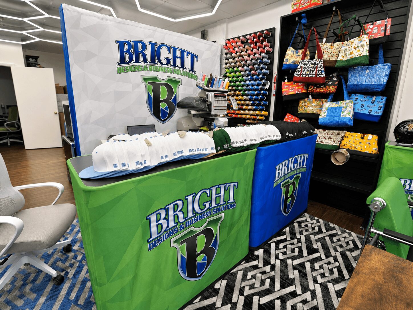 Display table with Bright logo, fabric rolls, and colorful bags in a store, with patterned floor and chairs nearby.
