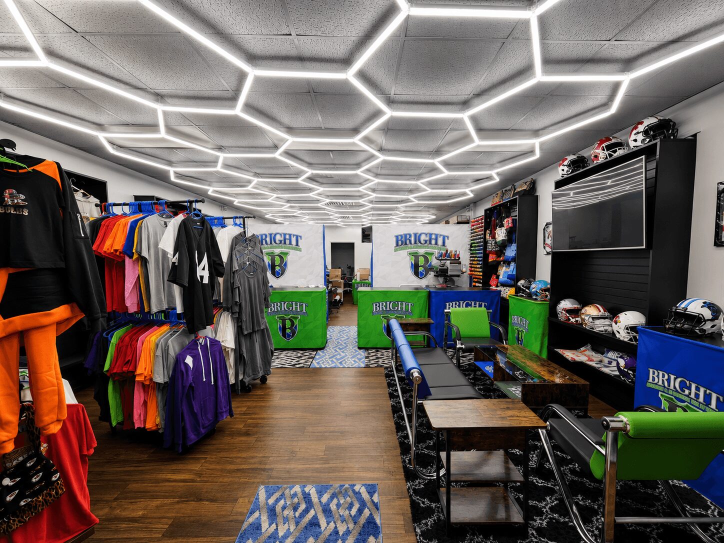 Clothing store interior with colorful shirts on racks, green and blue chairs, and a patterned ceiling. Word 'BRIGHT' visible on banners.