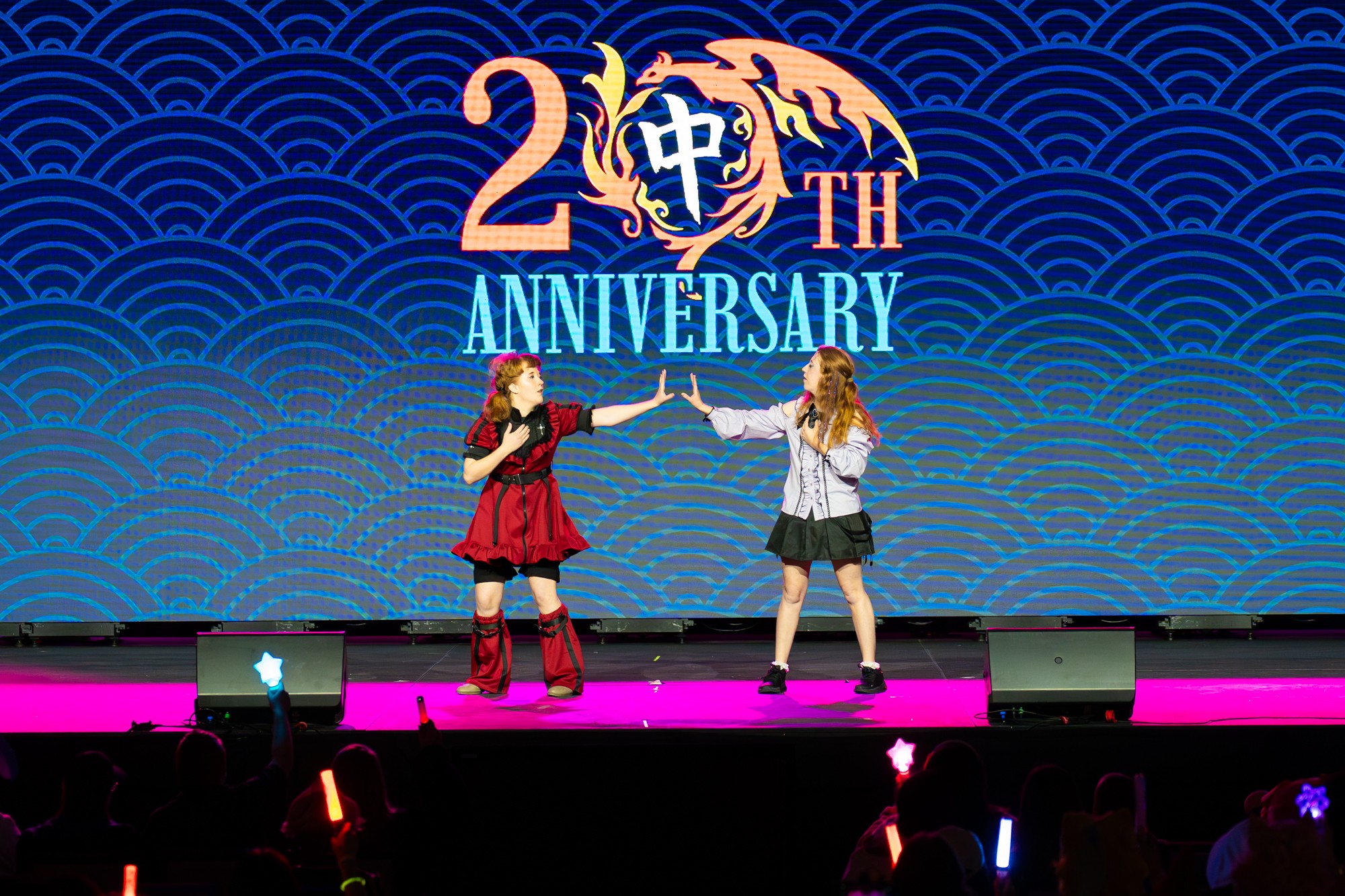Two people on stage exchanging a handshake in front of a large anniversary backdrop with a dragon and Chinese characters.