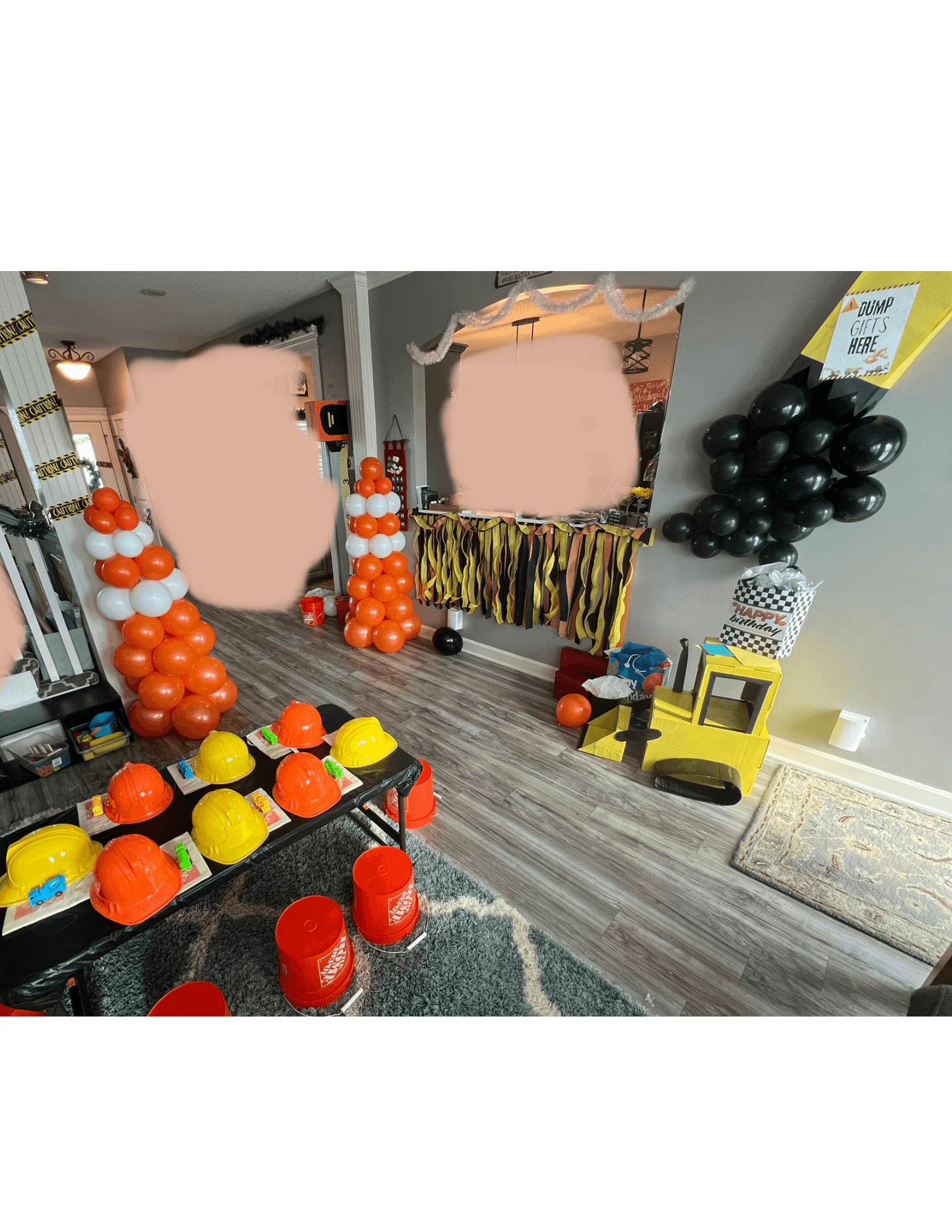 Party decorations with orange, yellow, and black balloons, a yellow toy, and a black and white patterned box, on a wooden floor.