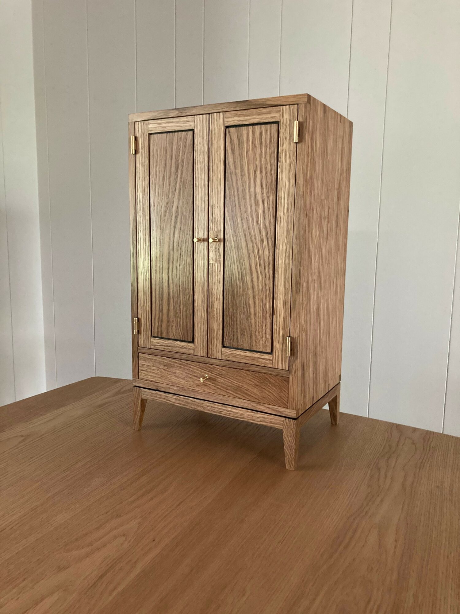 Wooden cabinet with two doors and a small open shelf, placed on a wooden floor against a white wall.