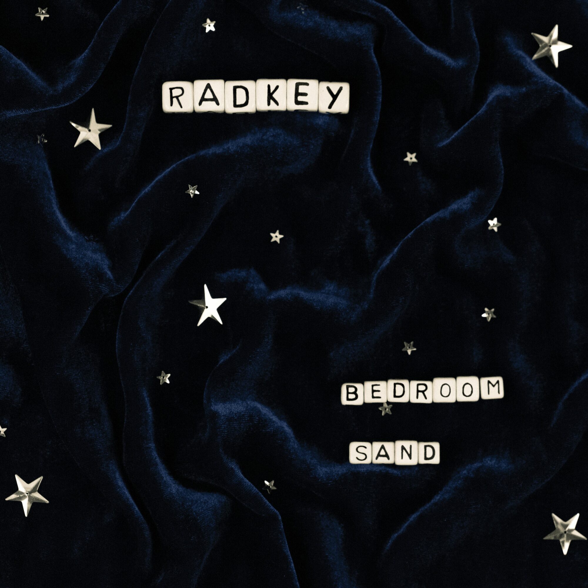 Dark blue fabric with white star decorations, spelling out 'RADKEY', 'BEDROOM', and 'SAND' with letter tiles.