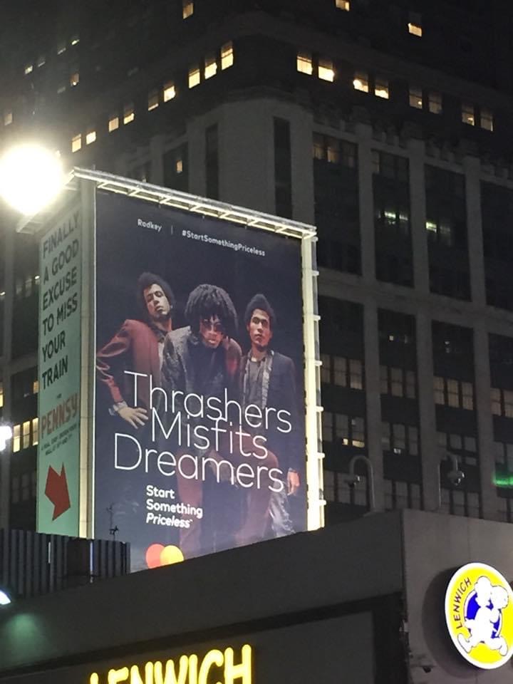Billboard featuring three people with text about Thrasher, Misfits, and Dreamers, against a city building background at night.