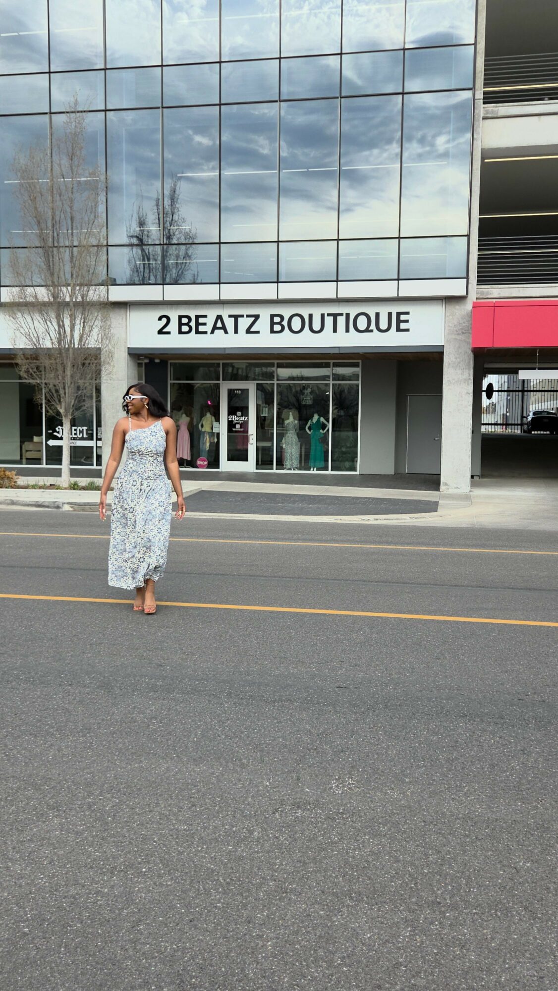 Person standing outside a boutique store with glass windows and a sign reading 'BEATZ BOUTIQUE'.