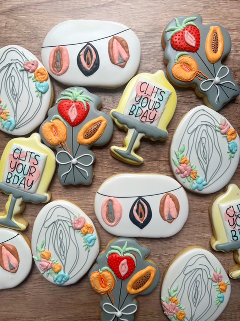 Assorted decorated cookies with strawberries, strawberries, strawberries, and text reading 'Clits your bday' on a wooden surface.