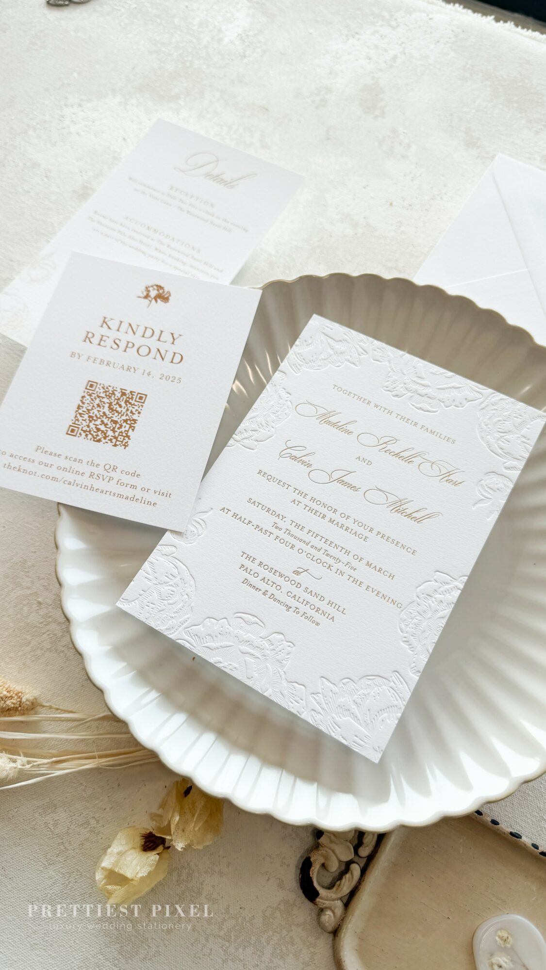 Invitation card with elegant script, placed on a white scalloped plate, with other papers nearby, on a light surface.
