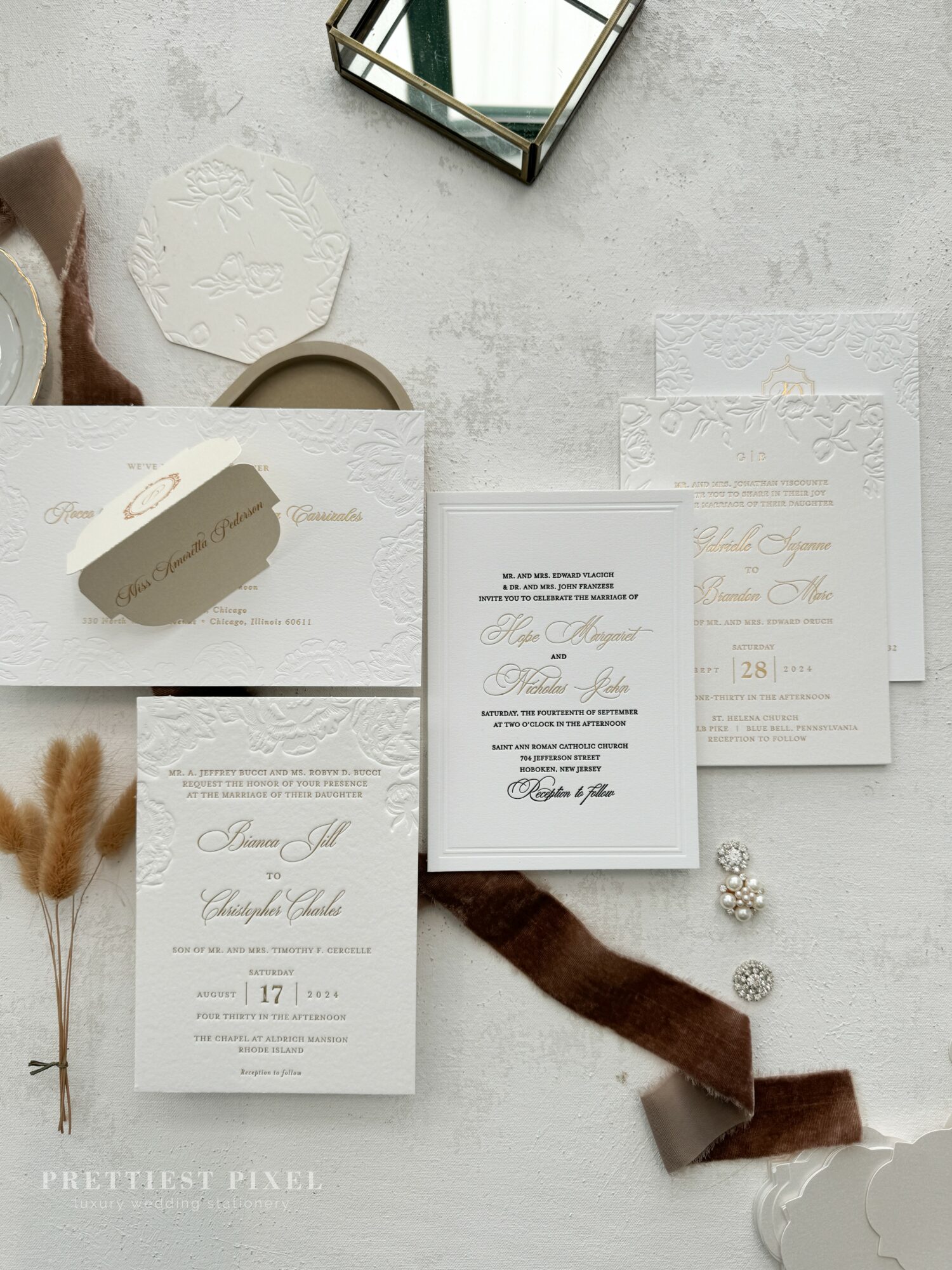 Flat lay of wedding invitations, a ring box, decorative items, and a mirror on a light surface.