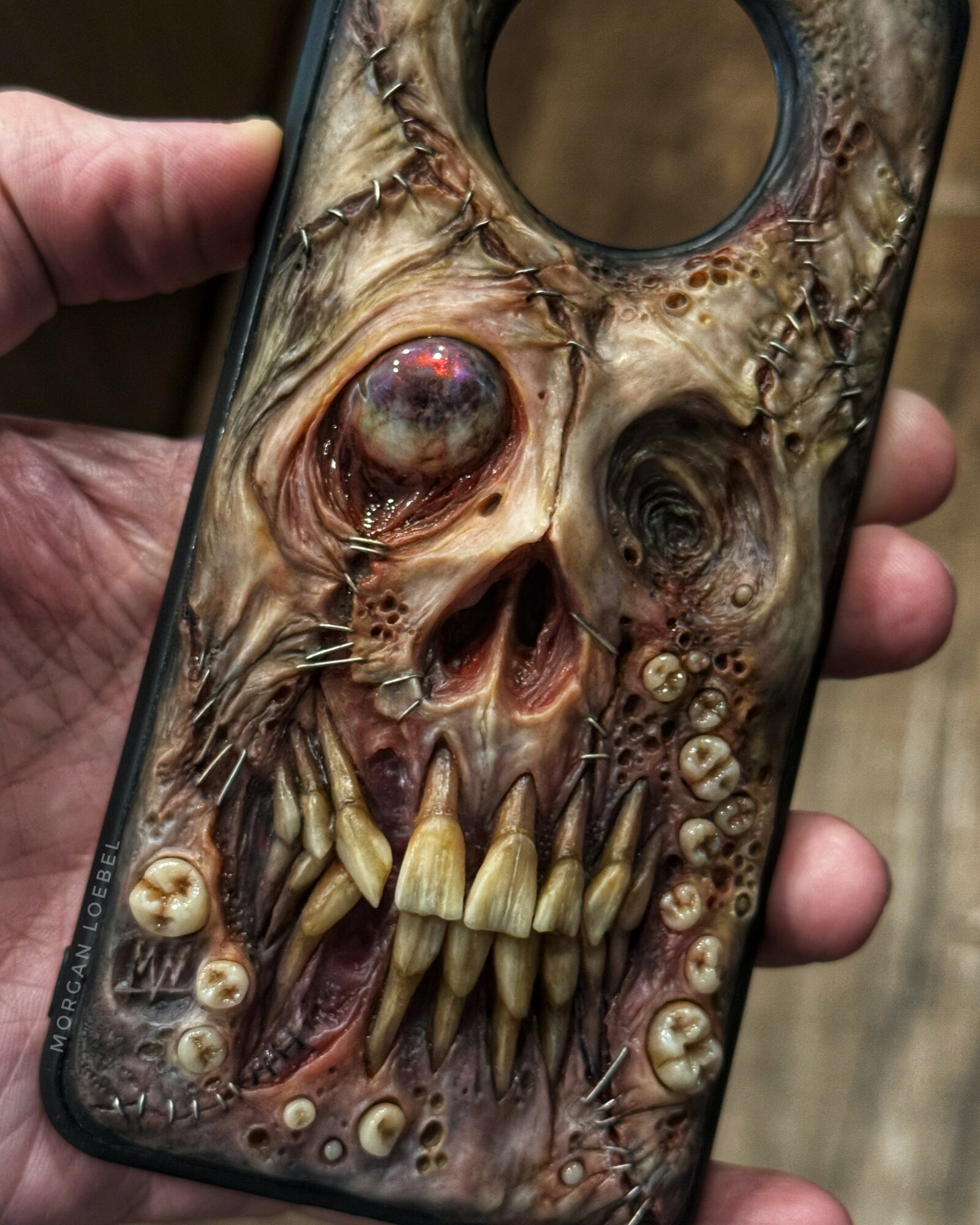 Phone case with a detailed, grotesque skull design featuring large eye, sharp teeth, and decayed features.