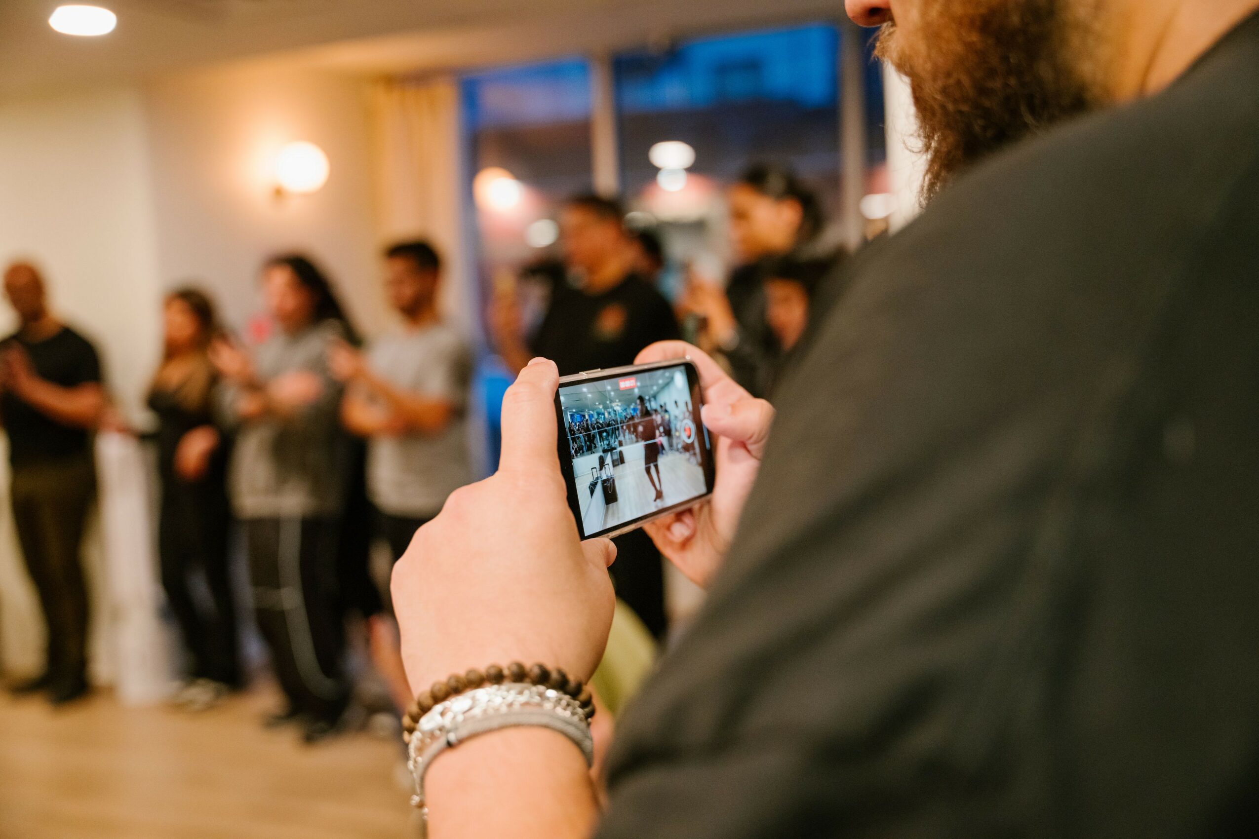 Person taking a photo with a smartphone at a social gathering indoors, with people in the background.