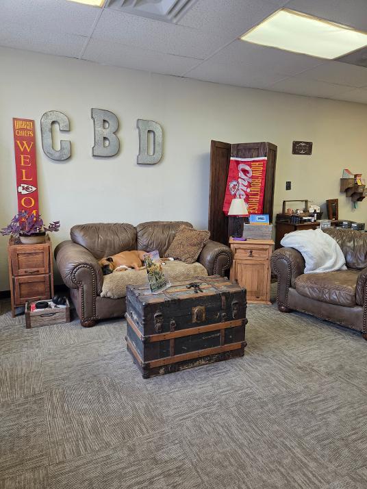 Living room with a brown leather sofa, a wooden chest, and a second sofa, with wall decorations including large letters and a Coca-Cola vending machine.