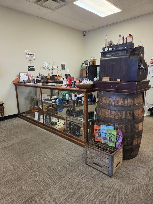 Display case with vintage items, a large wooden barrel, and a small crate with books in a room with plain walls and ceiling lights.