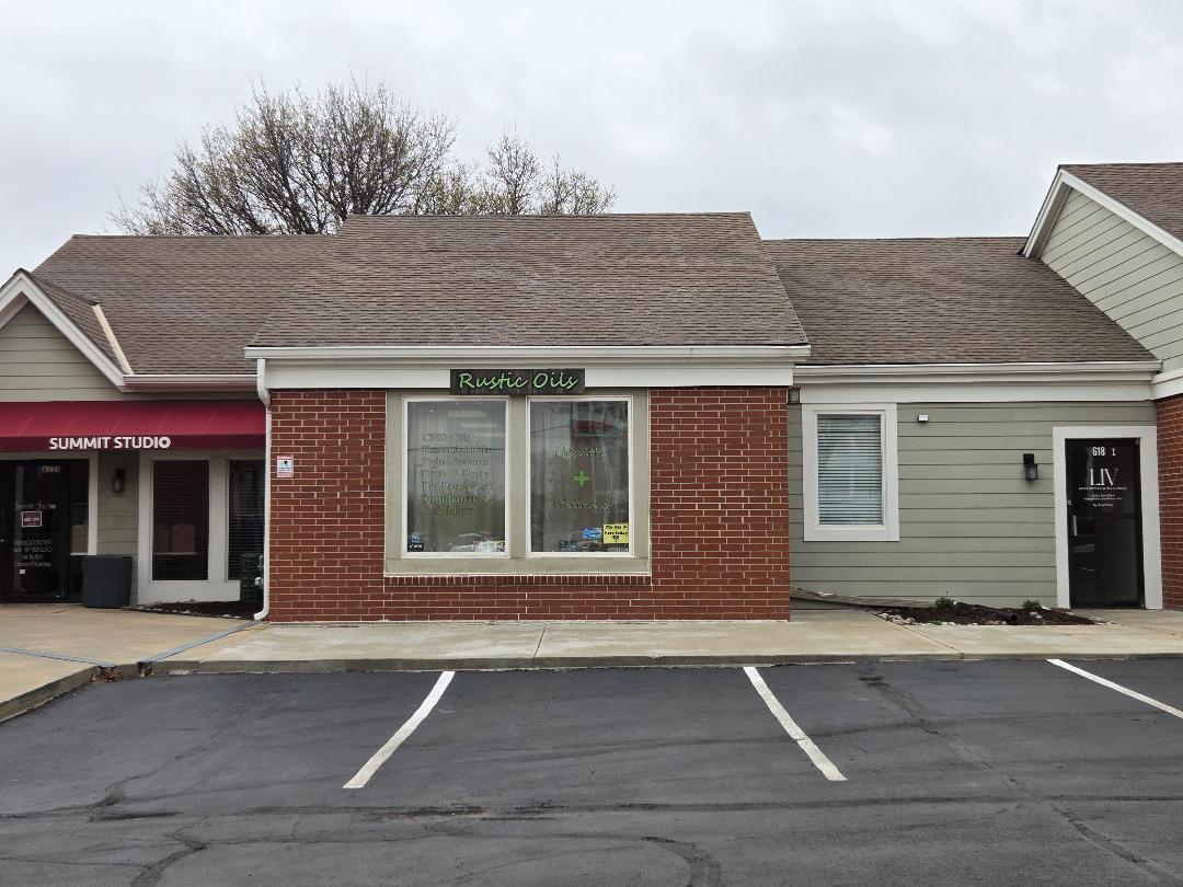 Front view of a building with brick and gray siding, parking spaces in foreground, cloudy sky, and trees in background.