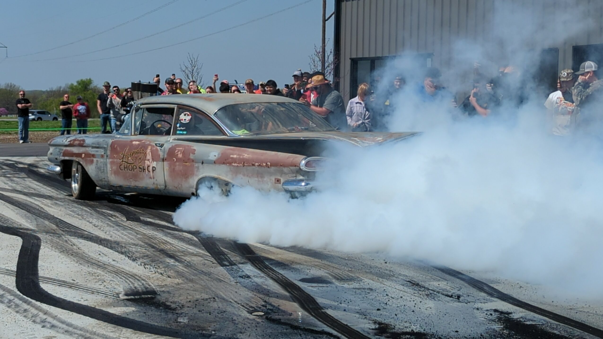 Vintage car emitting smoke on a racetrack with spectators in the background.