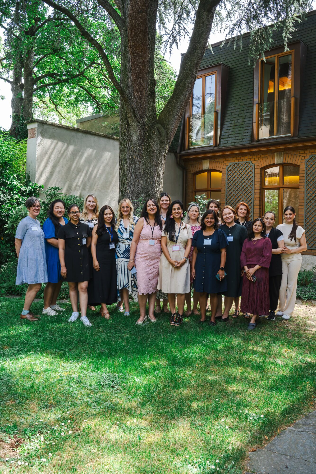 Group of women standing outdoors in front of a house with large windows and trees, smiling for the photo.