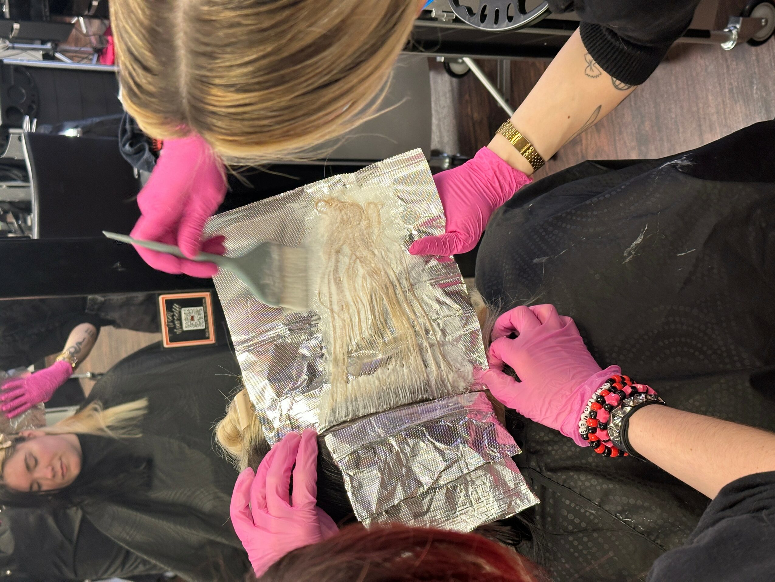 Person wearing pink gloves handling a foil-wrapped object, with another person in the background, in a room with dark flooring.