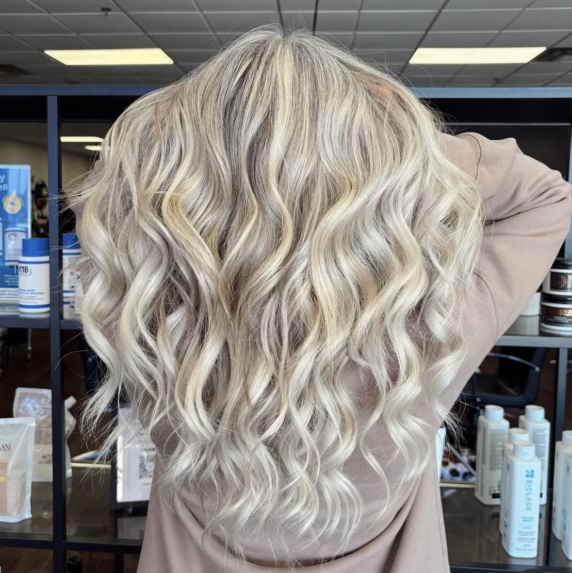 Person with long, wavy, blonde hair seen from behind in a store or salon setting.