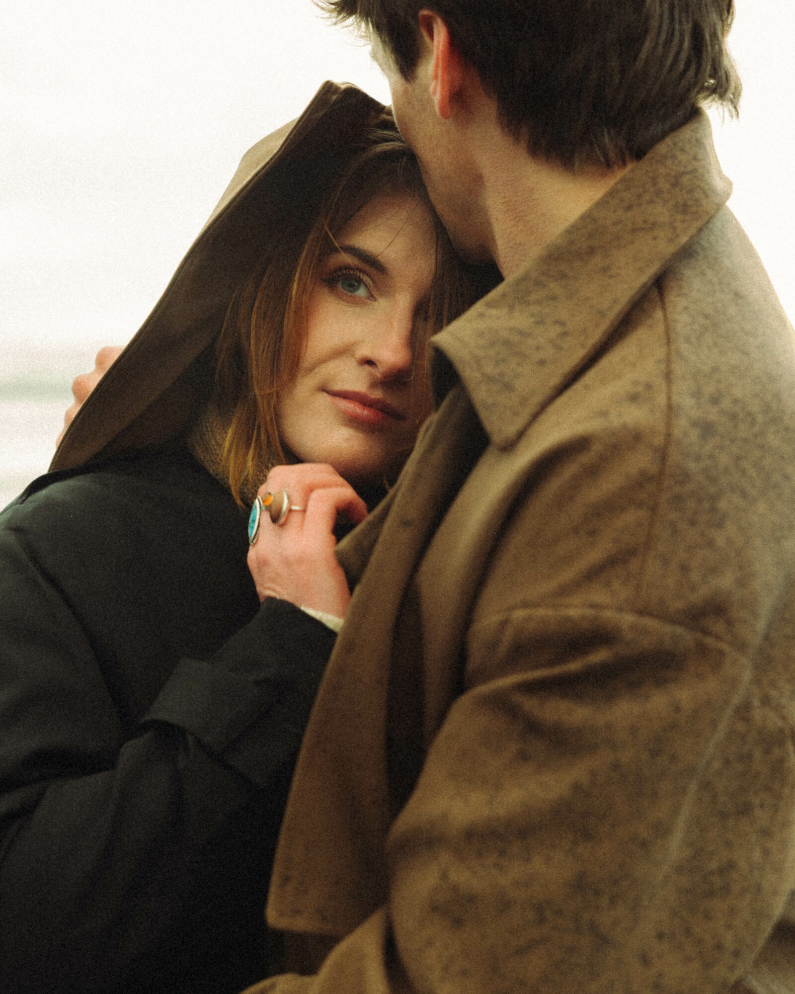 A woman with a hat and a man in a coat close together, looking at each other affectionately.