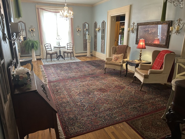 Elegant living room with chairs, a large rug, chandelier, and a window with curtains.