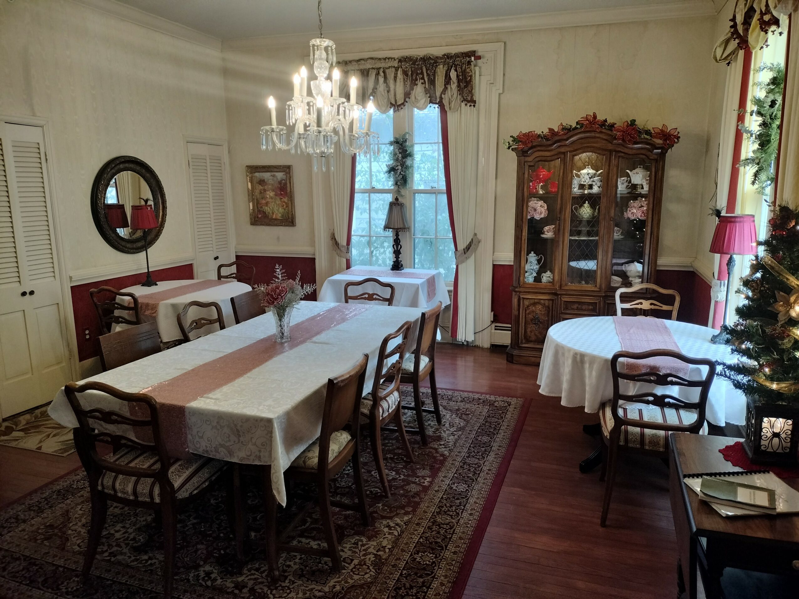 Dining room with a chandelier, large table, chairs, a china cabinet, and a window with curtains.