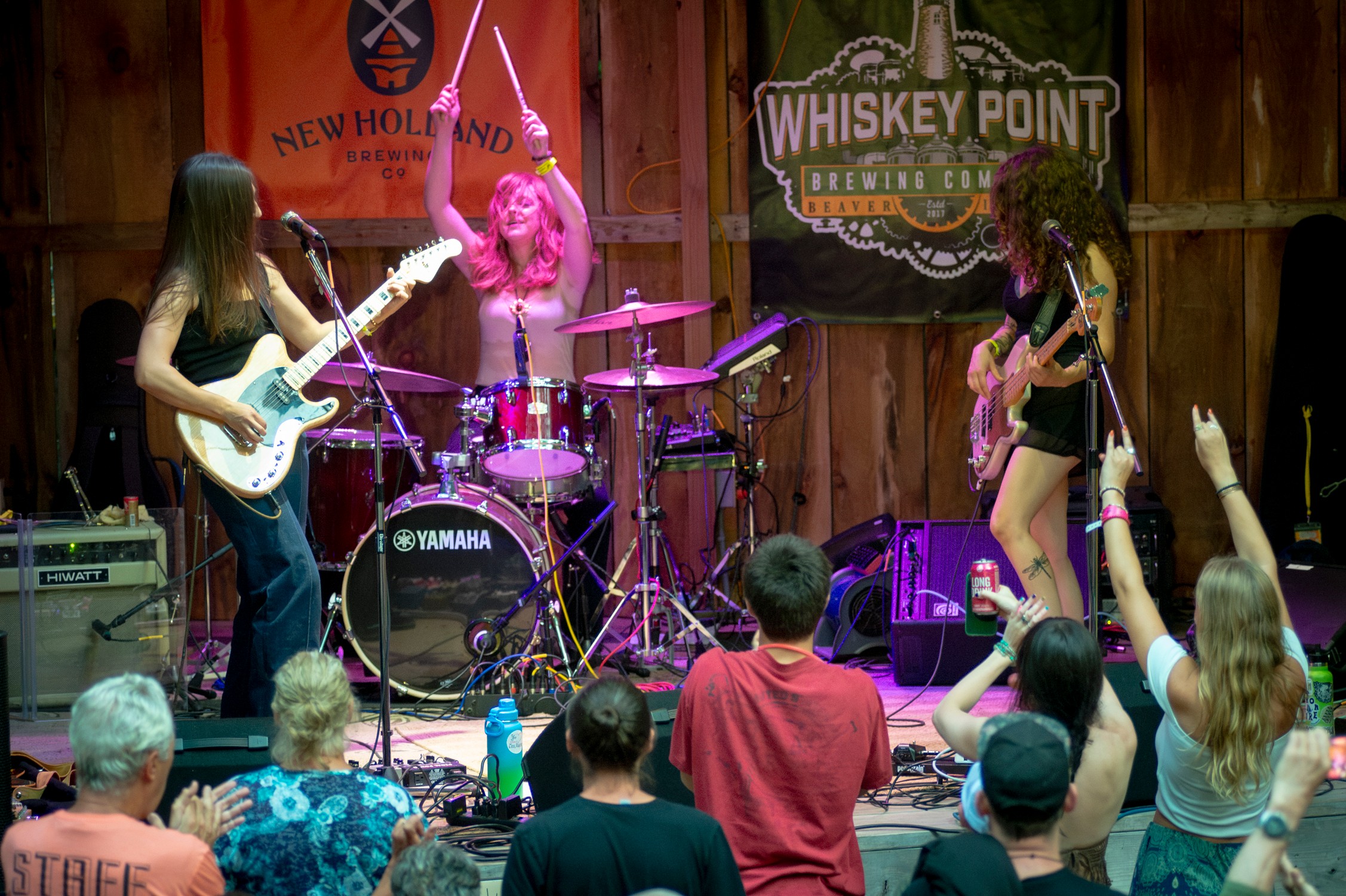 Three women perform on stage with musical instruments in front of an audience at Whiskey Point venue.