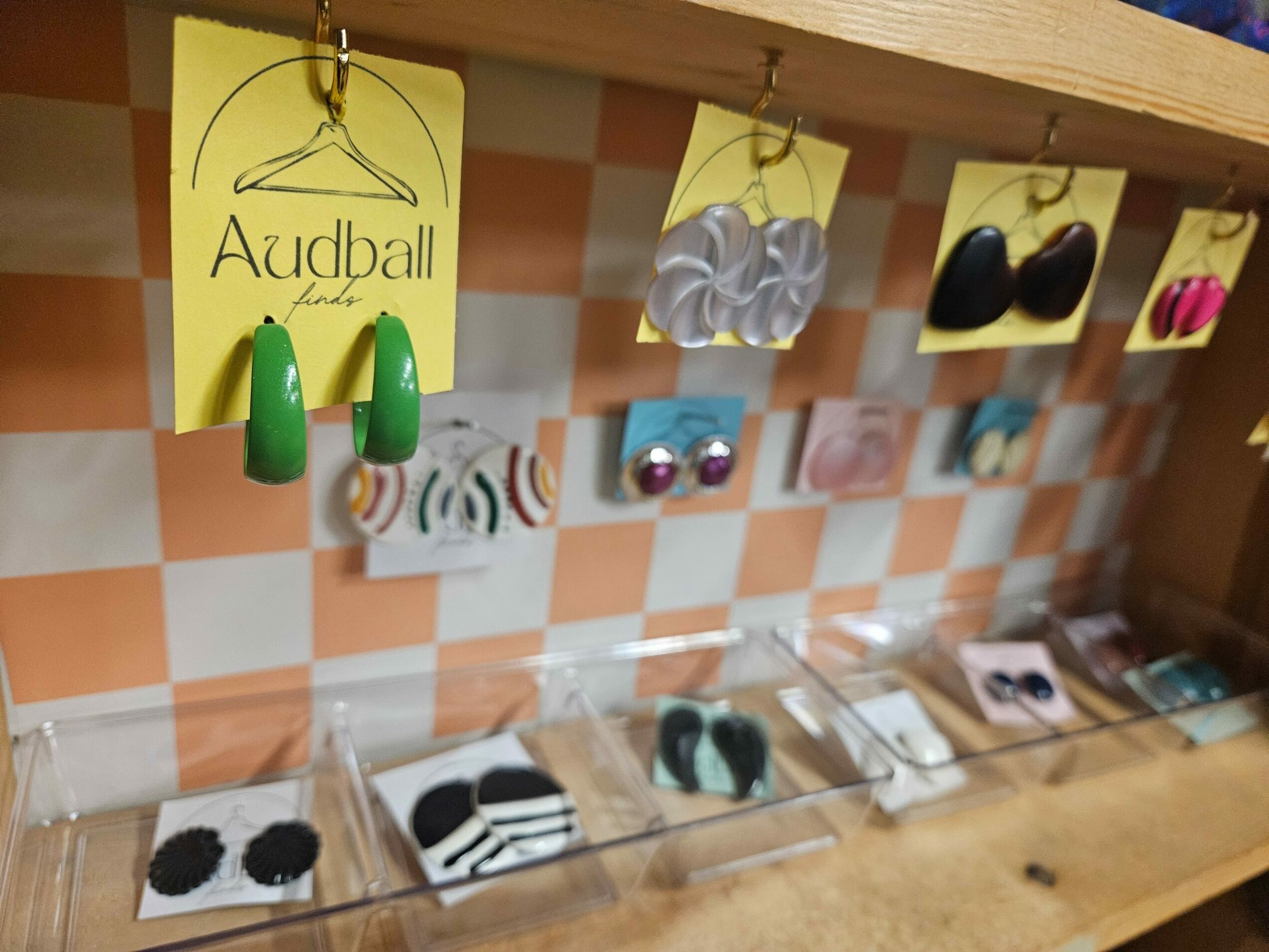 Display of various earrings on yellow cards, arranged on a checkered surface with a wooden background.